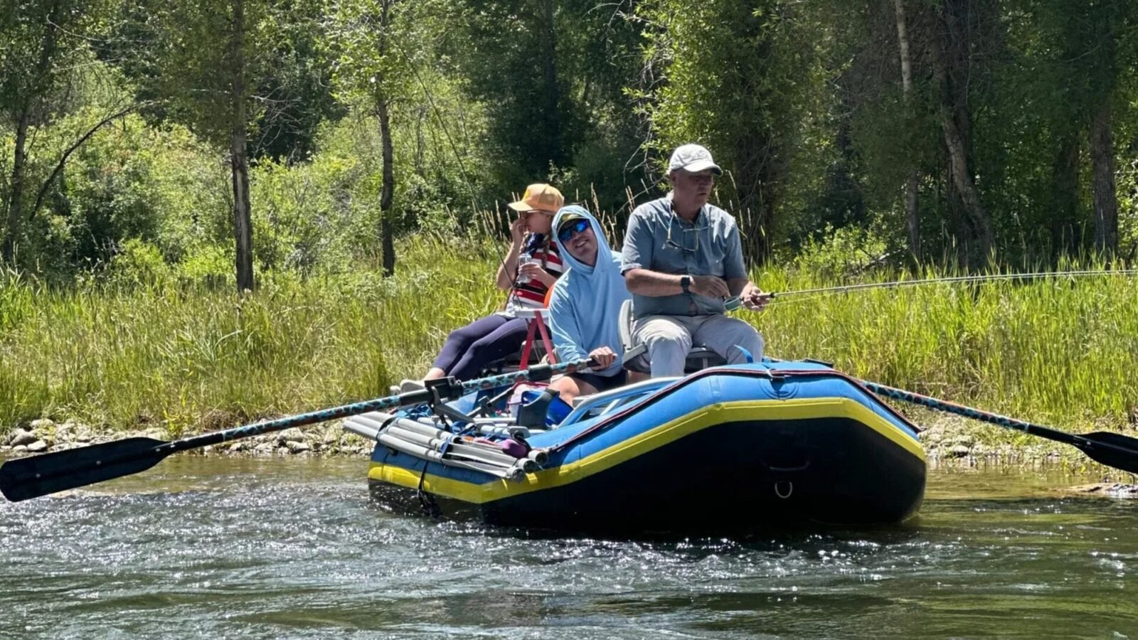 Three anglers fishing from a drift boat along a grassy river bank